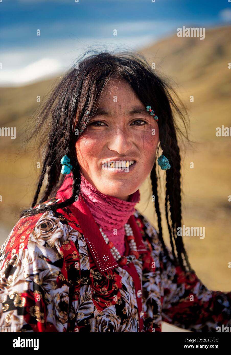 Eine junge Tibeterin trägt traditionellen Schmuck, der für ihre ethnische Gruppe typisch ist, sowie goldbedeckte Kaninchen, tibetisches Plateau Stockfoto