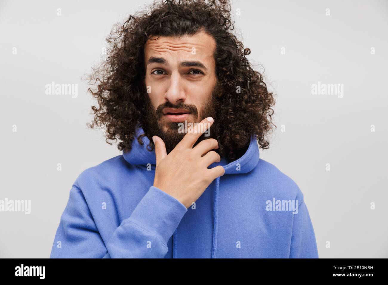 Bild eines nachdenklichen, unrasierten Mannes in legeren Sweatshirt, das aufschäumt und sein Kinn berührt, isoliert über weißem Hintergrund Stockfoto