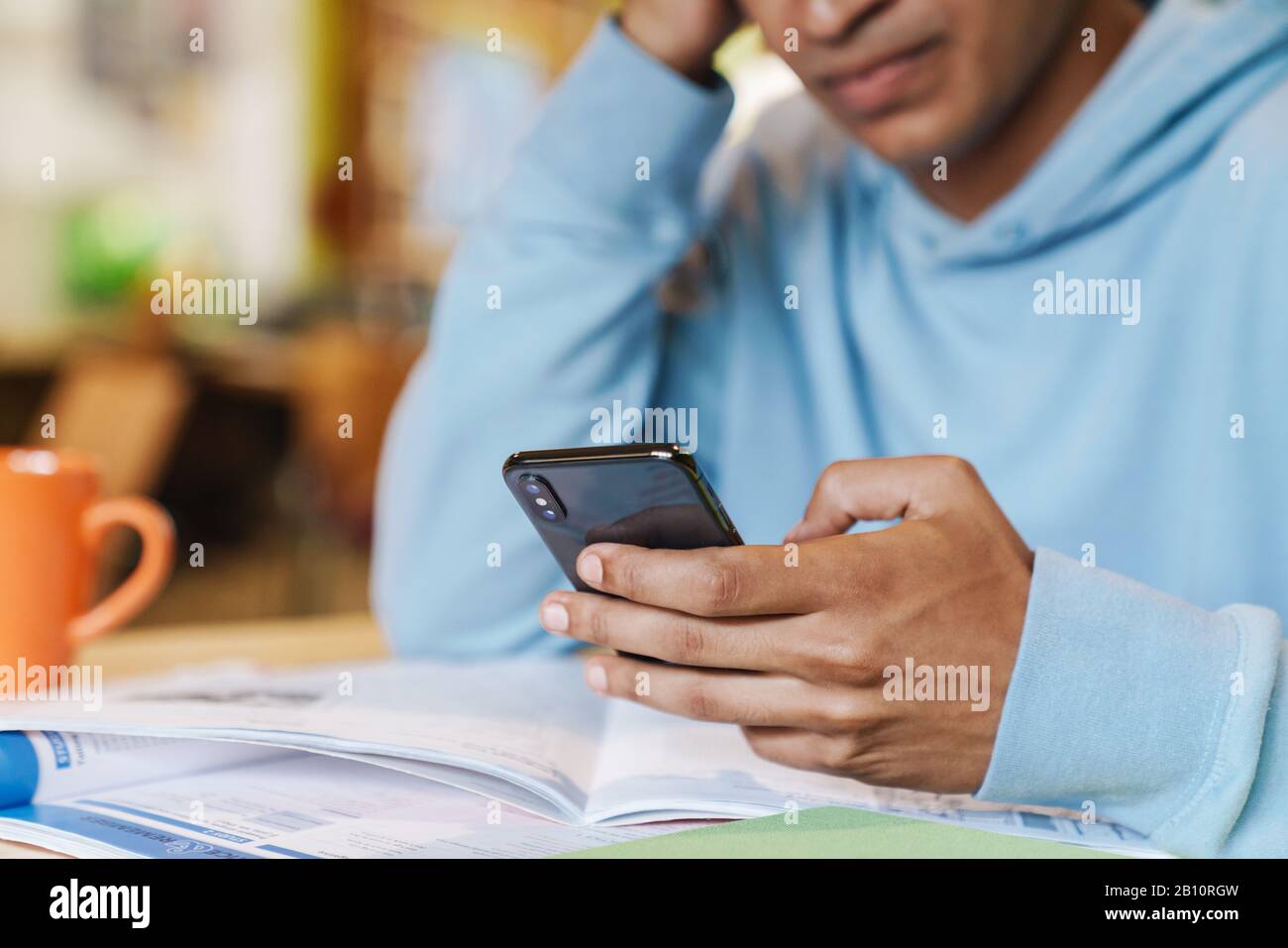 Nahaufnahme eines ernsthaften afrikanischen Jungen, der im Innenbereich mit dem Handy an der Drehscheibe sitzt Stockfoto
