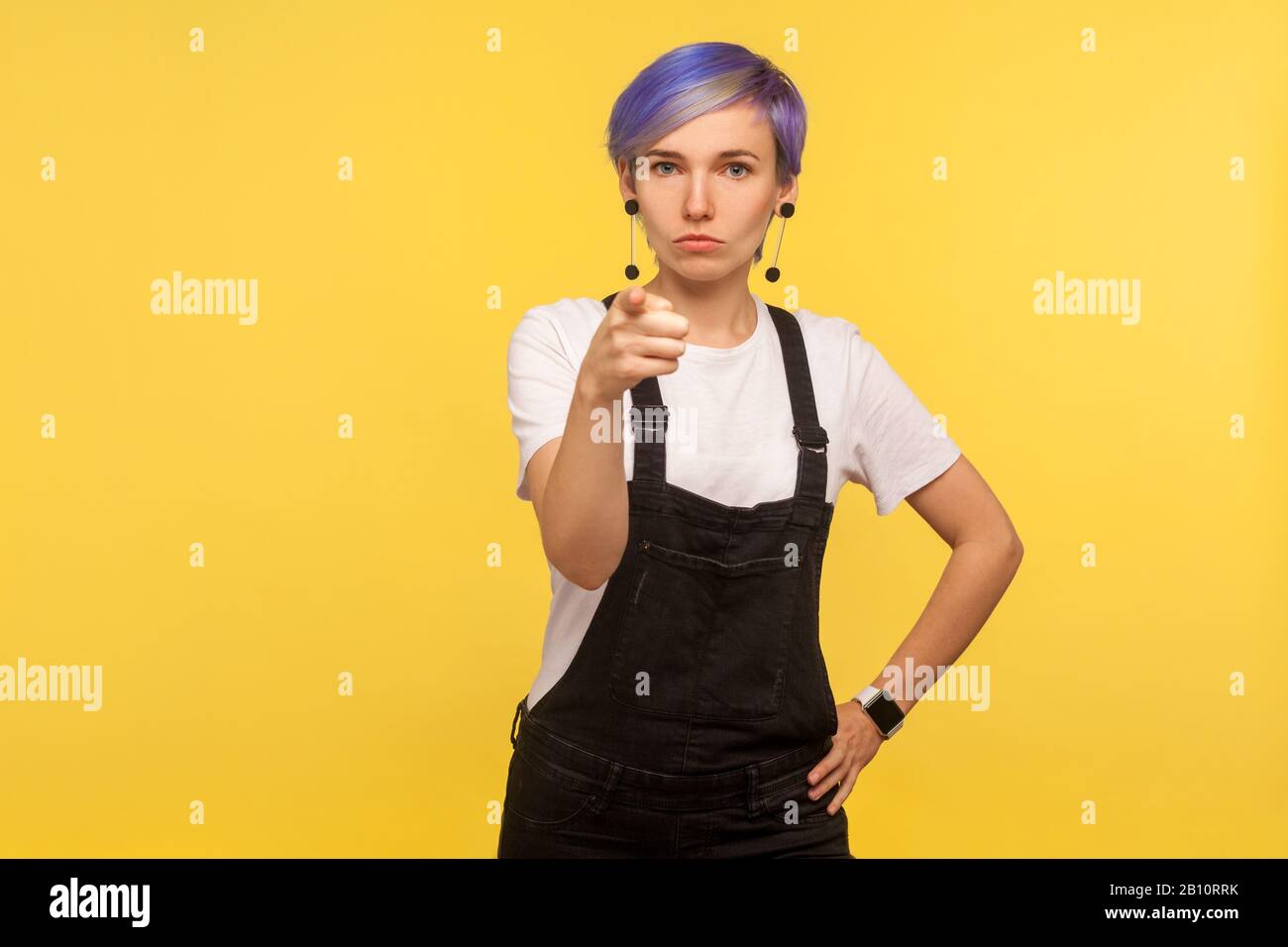 HE, du! Porträt der Hüpffrau mit violettem, kurzem Haar in Denim-Overalls, die auf die Kamera zeigen und streng starr aussehen, die Wahl treffen mit seriösem fa Stockfoto