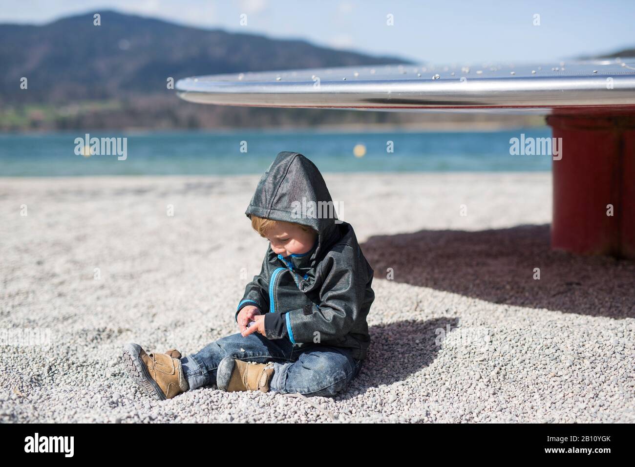 Der kleine Junge sitzt am Strand an einem See Stockfoto