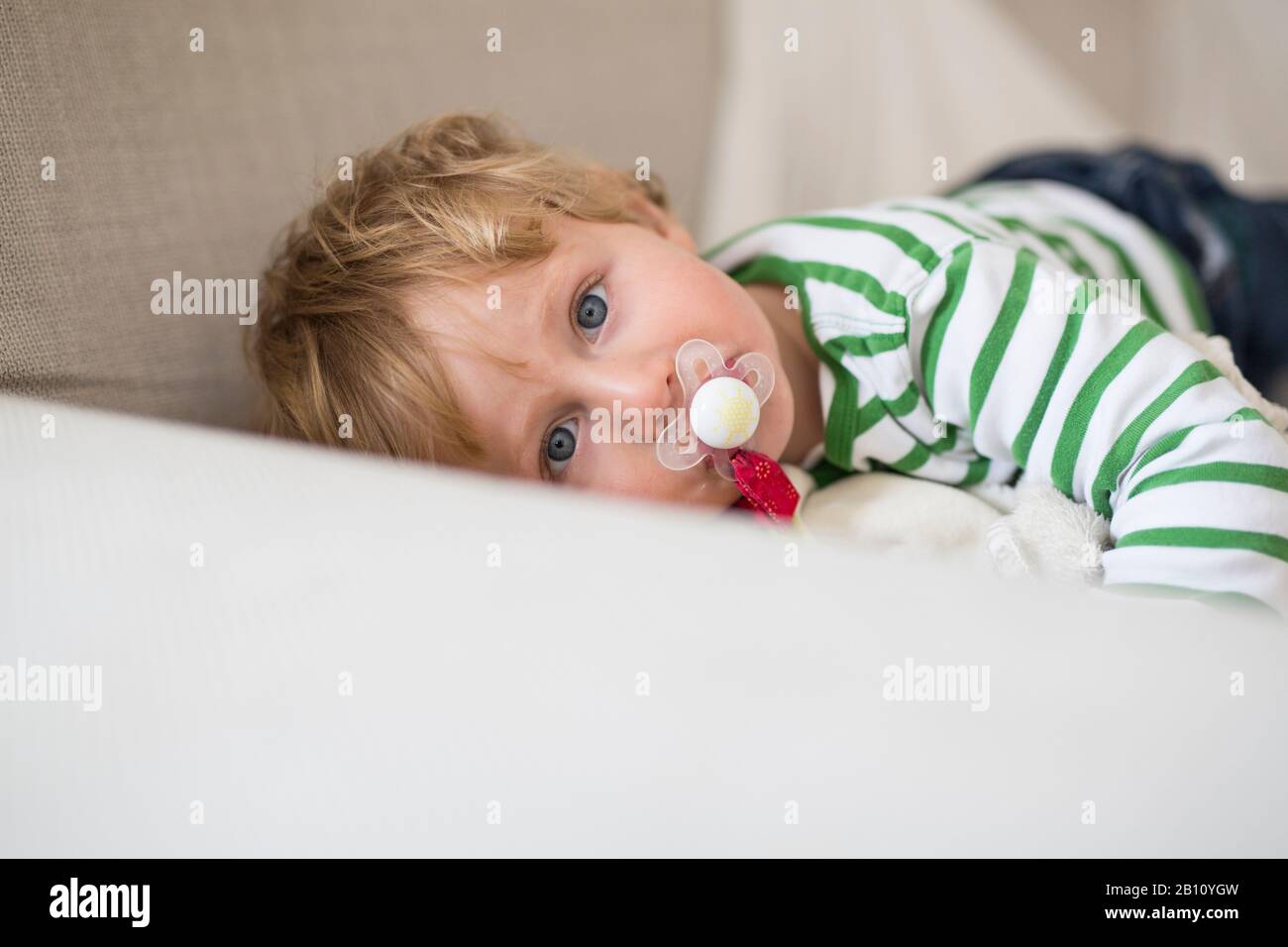 Kleiner Junge mit Schnuller liegt auf dem Sofa Stockfoto
