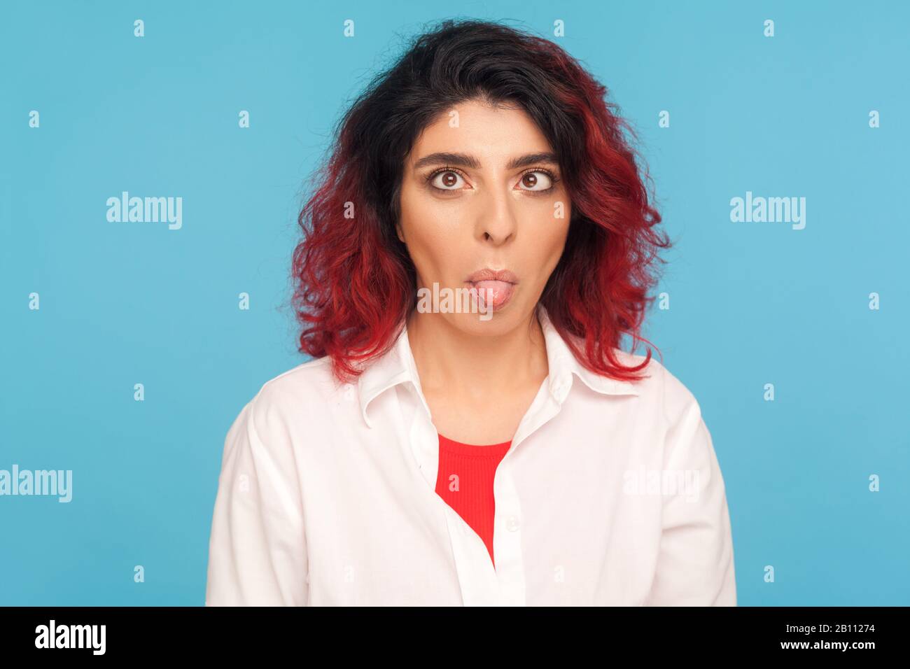 Porträt einer dummen Hüftfrau mit ausgefallenen roten Haaren, die die Augen durchqueren und die Zunge herausstechen, mit dummem, brainlosem Ausdruck getäuscht. IND Stockfoto