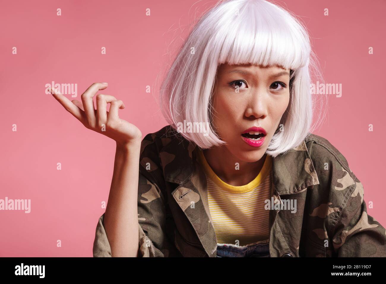 Bild eines empörten asiatischen Mädchens, das weiße Perücke trägt, die in der Empörung über rosafarbenem Hintergrund verärgt und gestikuliert wurde Stockfoto