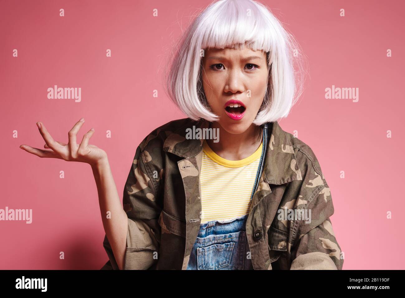 Bild eines empörten asiatischen Mädchens, das weiße Perücke trägt, die in der Empörung über rosafarbenem Hintergrund verärgt und gestikuliert wurde Stockfoto
