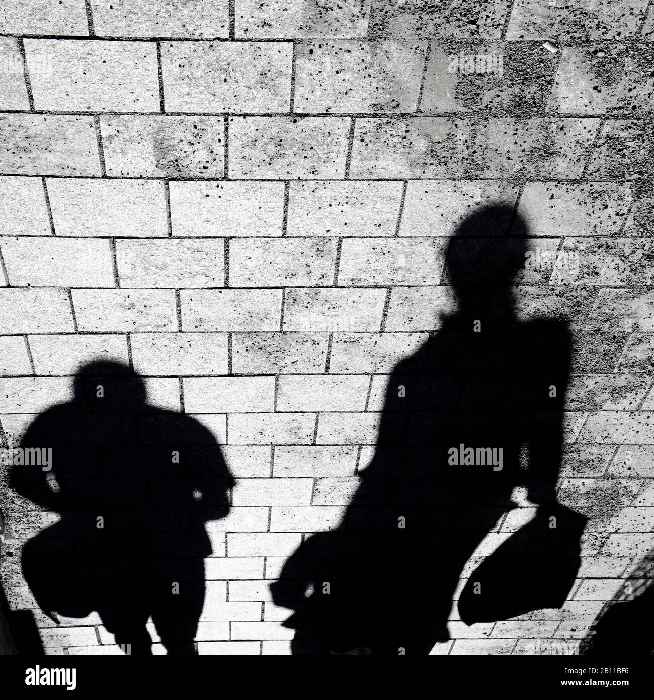 Verschwommene Schattensilhouette von Menschen, die auf Bürgersteigen in der Stadt in kontrastreicher Schwarz-Weiß-Farbe auf dem Kopf laufen Stockfoto