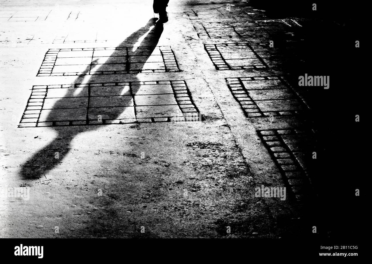 Verschwommene Schattensilhouette eines Mannes, der in der Nacht allein auf dem Bürgersteig der Stadt in Schwarzweiß spazieren ging Stockfoto