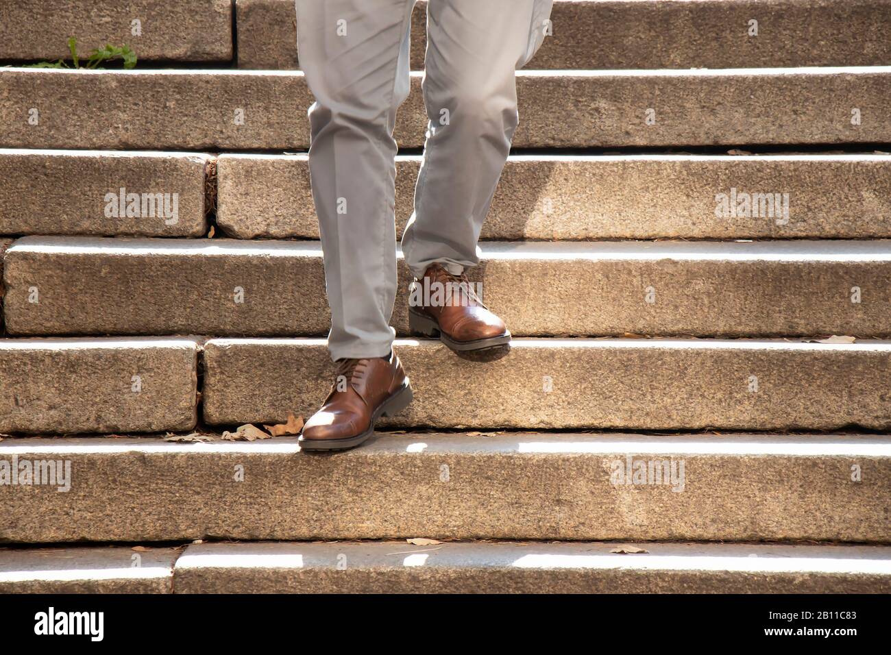 Ein Mann in braunen Schuhen, der im Herbst bei Sonnenlicht die öffentliche Außentreppe hinunter spazieren ließ, Details seiner Beine in Bewegungsunschärfe Stockfoto