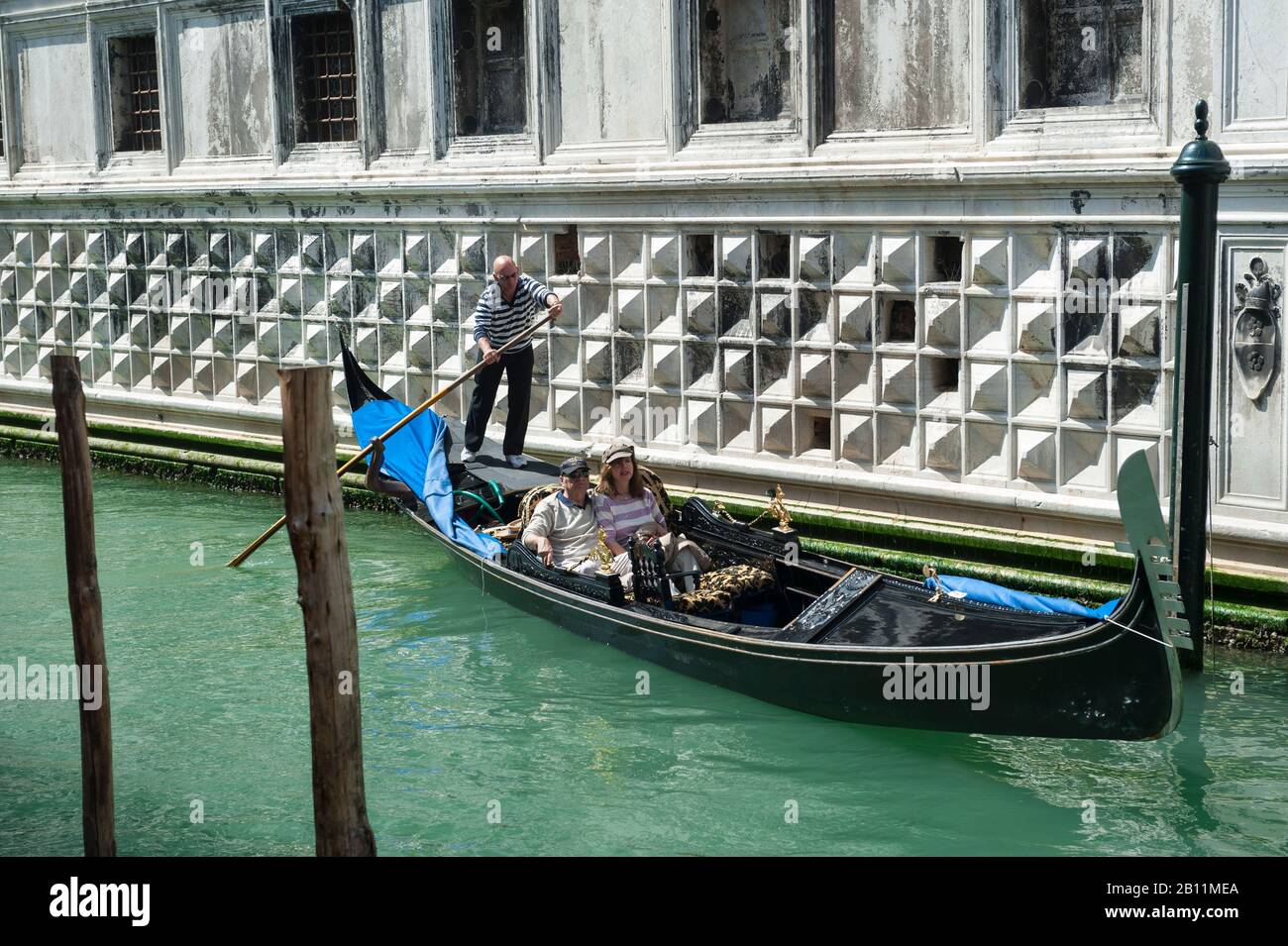 Venedig - 18. APRIL 2013: Ein Venezianer Gondolier manövriert ein Paar Touristen in einer Gondel entlang eines Kanals neben der Sala della Cancelleria Segreta. Stockfoto