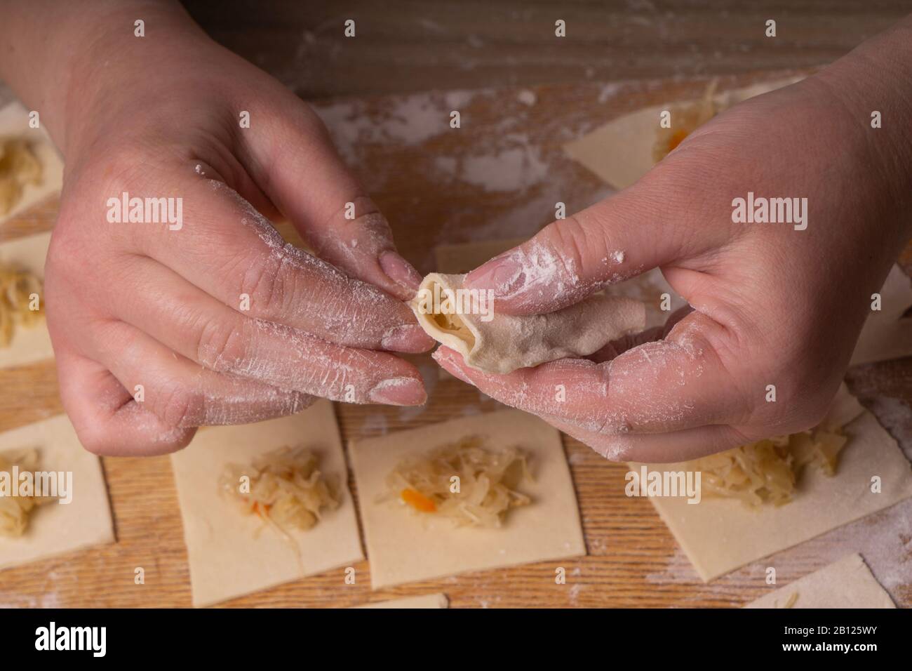 Eine Frau sculpt Knödel und Ravioli aus Kneten und Kohl. Sperrholzschneidplatte, Holzmehlsieb und Walzstift aus Holz - Werkzeuge für Stockfoto