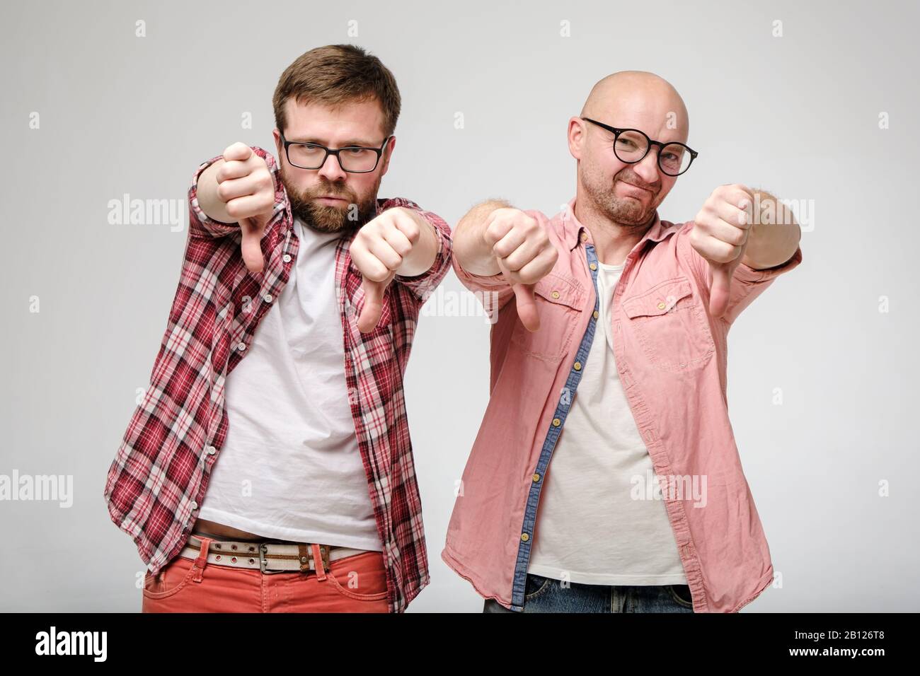Zwei Männer, die ein schlechtes Zeichen und eine Abneigung zeigen, machen eine Geste mit Daumen nach unten, mit einem grimace der Missbilligung auf ihren Gesichtern. Stockfoto