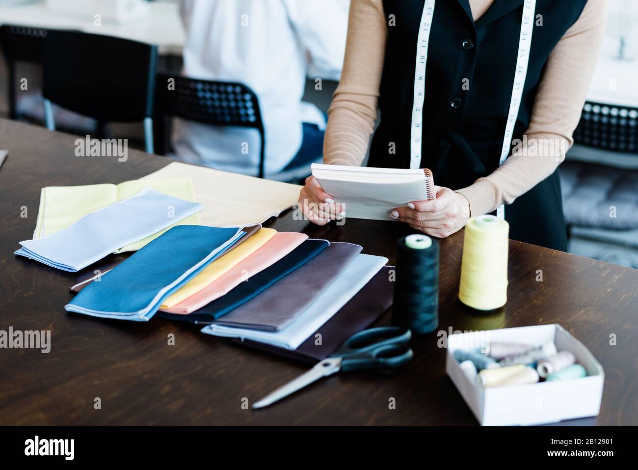 Hände junger, eleganter Designer mit Notizblock über Tisch, der mit Textil arbeitet Stockfoto