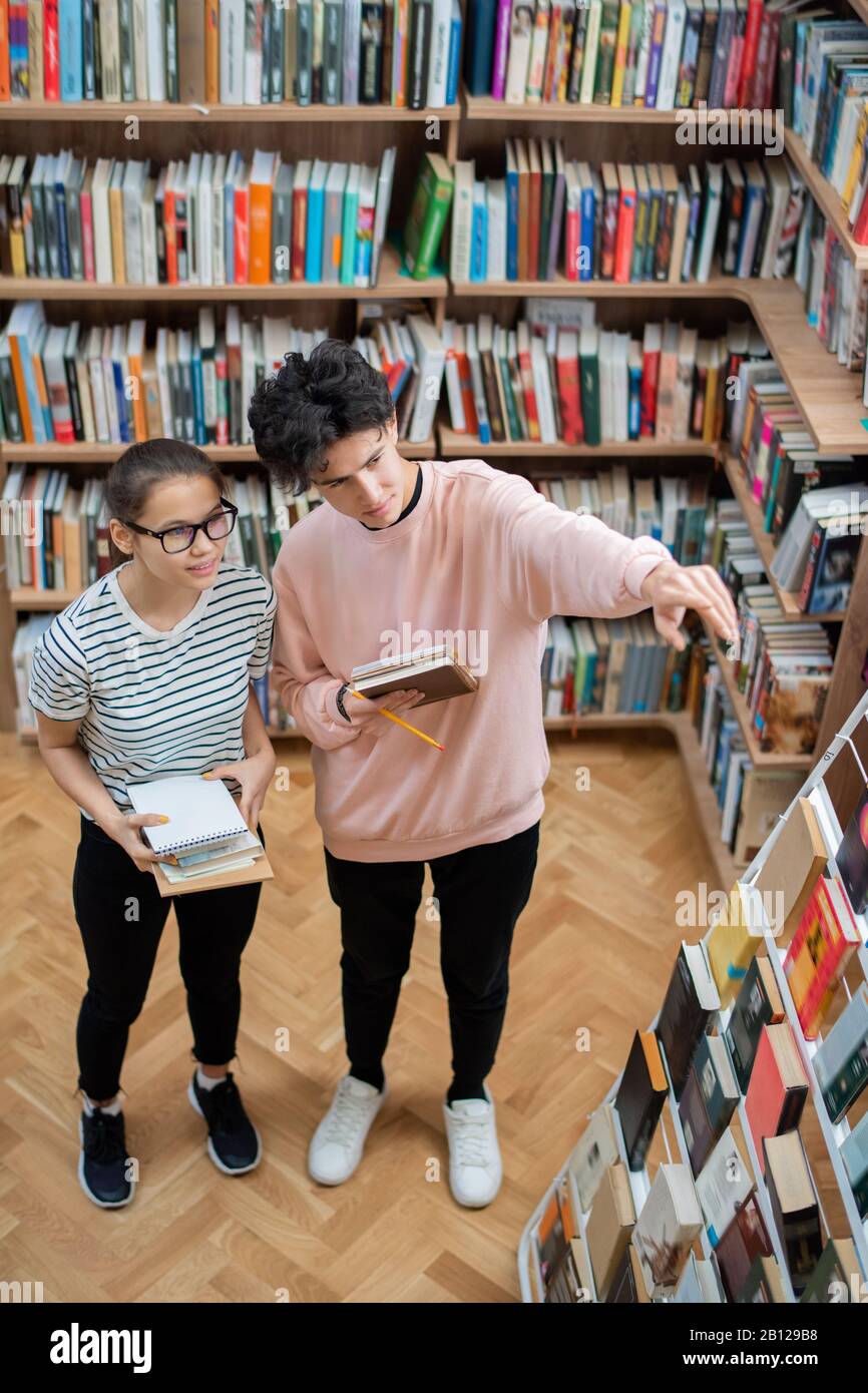 Zwei legere Teenager, die Bücher aus dem Bücherregal in der Hochschulbibliothek wählen Stockfoto