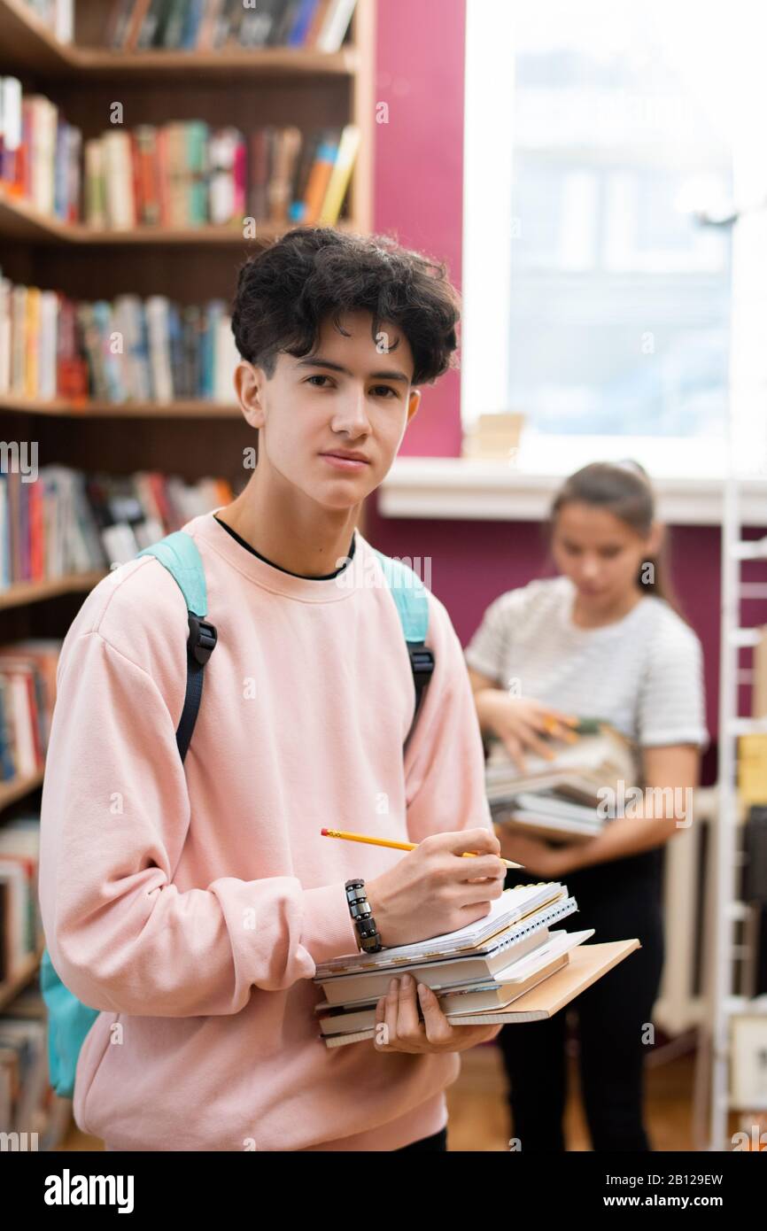 Teenager mit Rucksack, Stapel von Büchern und Bleistift in der College-Bibliothek Stockfoto