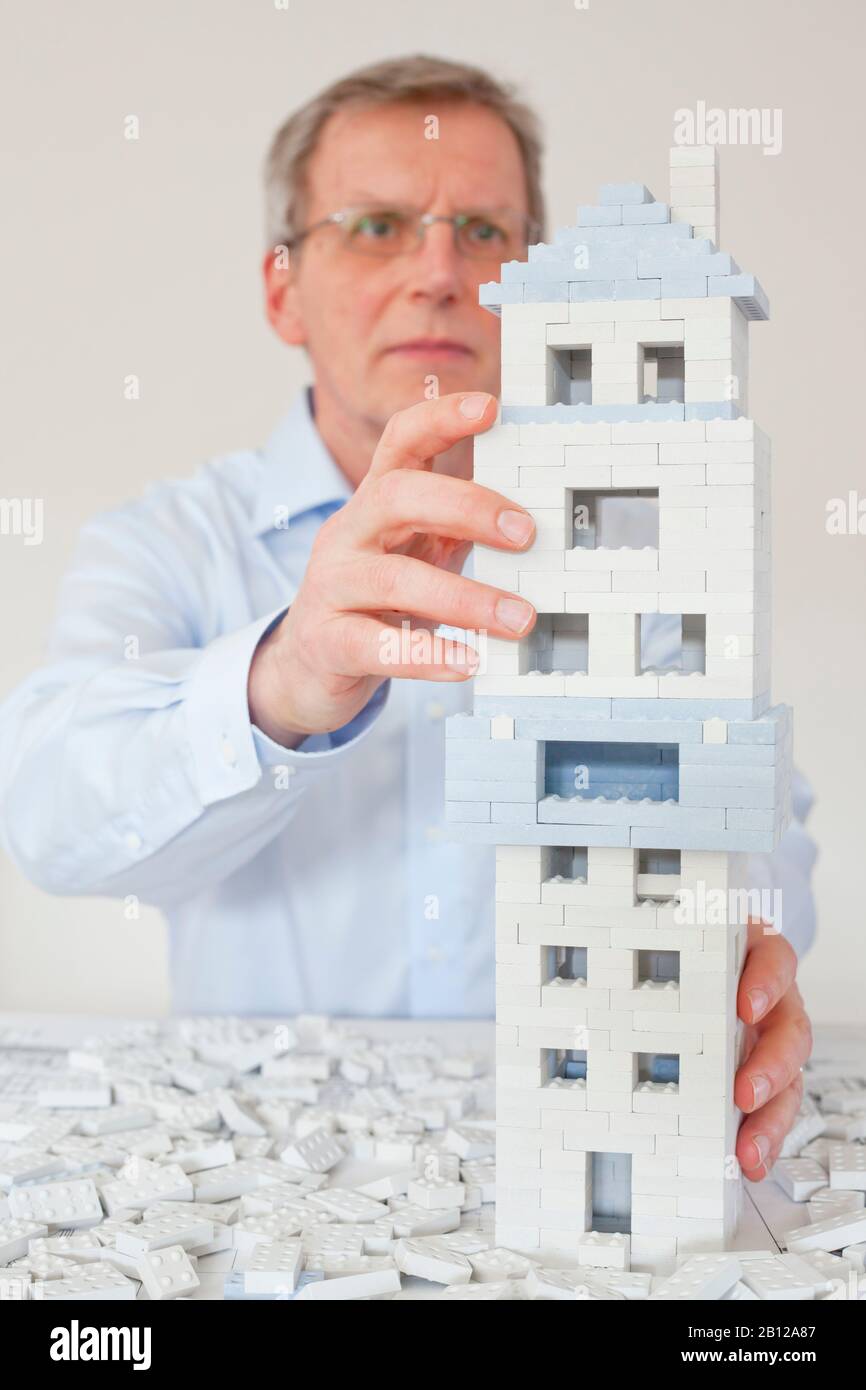 Reifer Architekt, der ein Haus mit Spielzeugblöcken untersucht Stockfoto