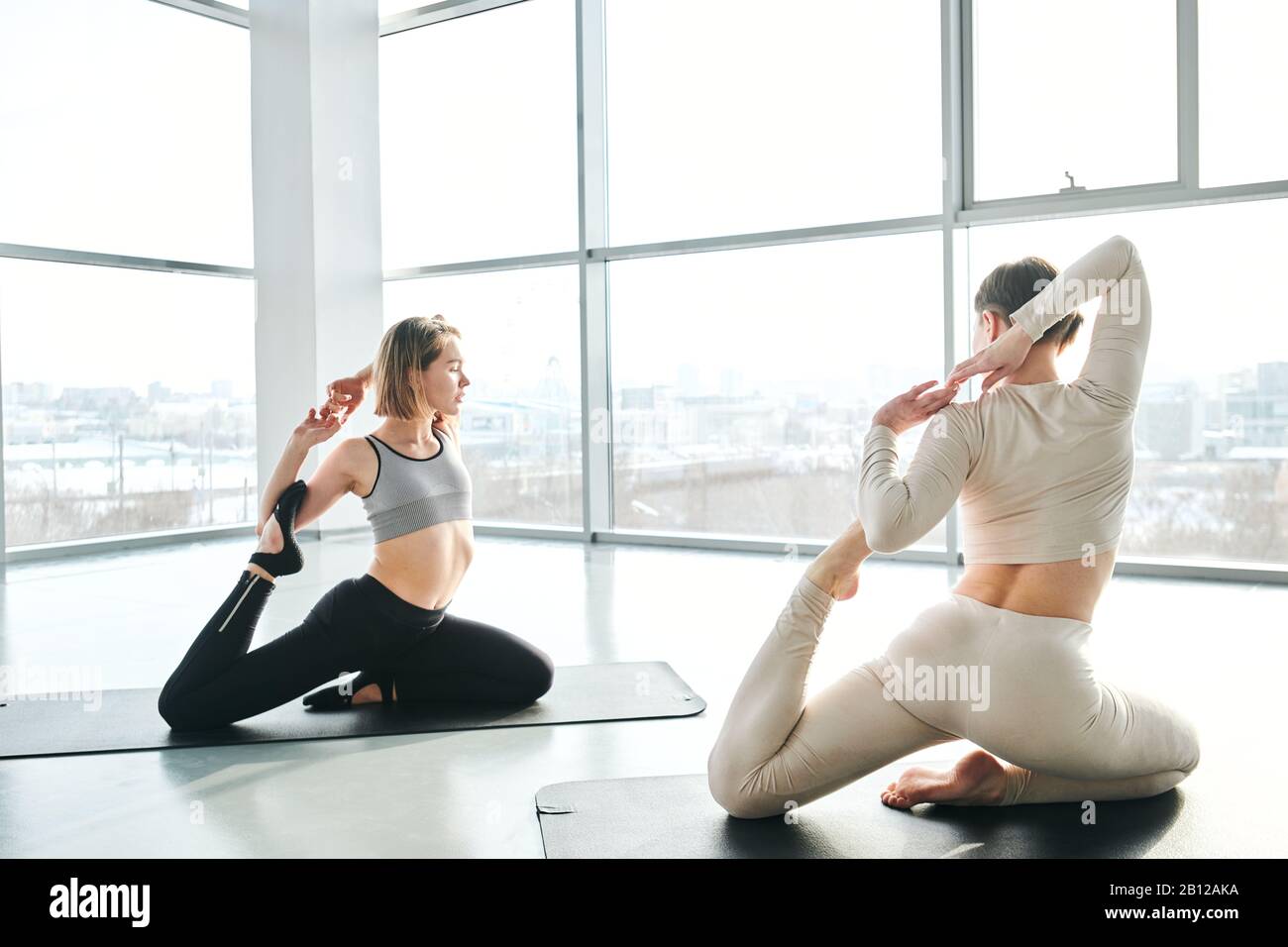 Junge aktive Frau, die nach ihrem Fitness-Trainer Yoga-Übungen wiederholt Stockfoto