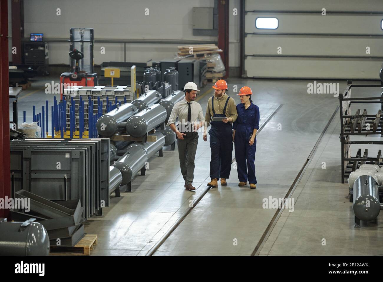 Gruppe von modernen professionellen Technikern in der Arbeitskleidung, die sich entlang der Werkstatt bewegen Stockfoto