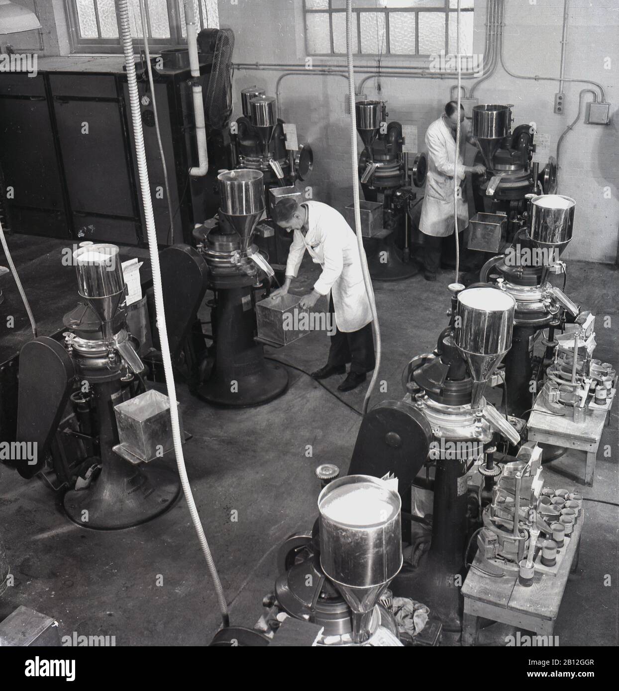 1950er Jahre, historische, weiß gestrichene männliche Arbeiter bei den Medizinprodukteherstellern von Arthur Cox & Sons in Brighton, England, Großbritannien, stehend an medizinischen Tabletten oder Pillenmaschinen der Ära. Stockfoto