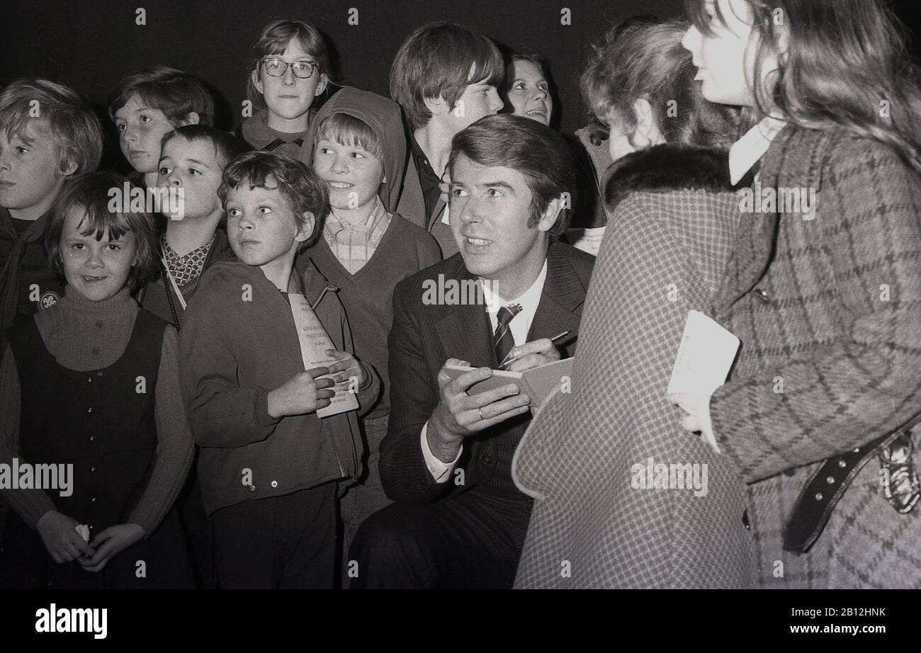 1960er Jahre, historischer, britischer Fernsehmoderator und Entertainer, Leslie Crowther bei einer Wohltätigkeitsfete, umgeben von Kindern, während er Autogramme zeichnet, London, England, Großbritannien. Er war unter jungen Leuten bekannt dafür, dass er TV-Programme für Kinder wie "Crackerjack" und "Meet the Kids" und Radioshow "Junior Choice" präsentierte. Stockfoto