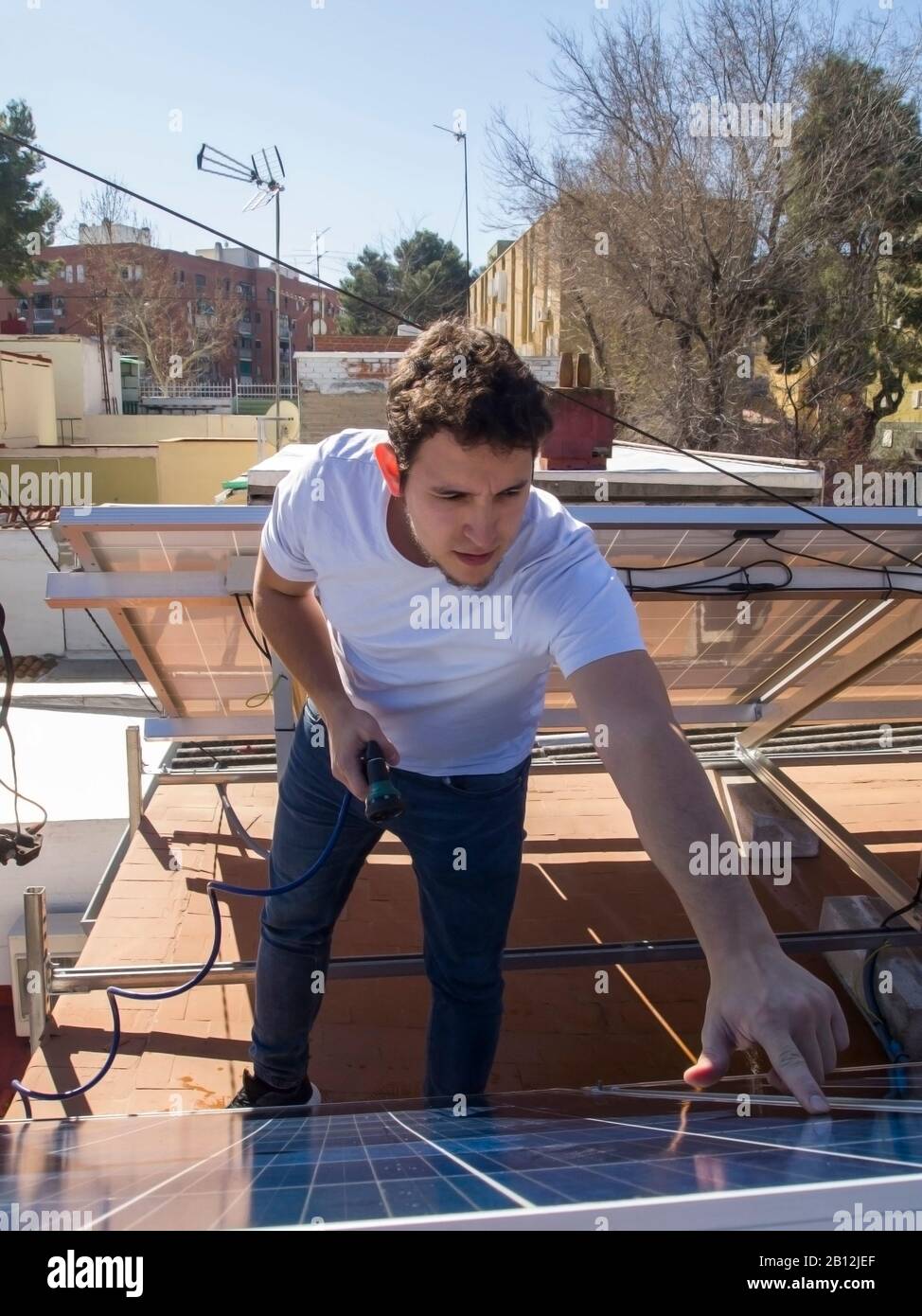 Kaukasisch attraktiver junger Mann, der Solarpaneele mit einem Schlauch überprüft und gereinigt. Alternative Stromquelle, nachhaltige Ressourcenkonzeption. Stockfoto