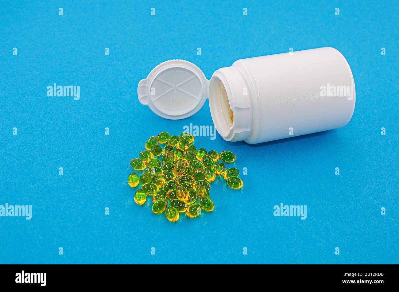Gelbe Pillen aus einem weißen Behälter auf blauem Hintergrund Stockfoto
