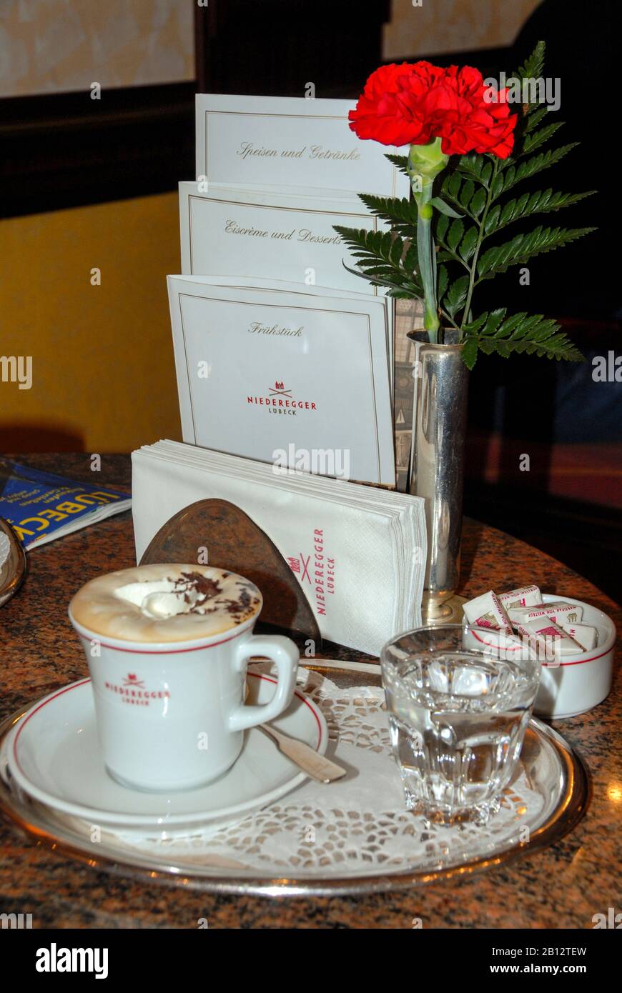 Eine Tasse Kaffee und ein Glas Wasser mit einer Rose in einer kleinen Vase wird im Kaffee-/Teesaal im Lübecker Marzipan (Lübeck Marzipan) Shop und in der Bar c serviert Stockfoto