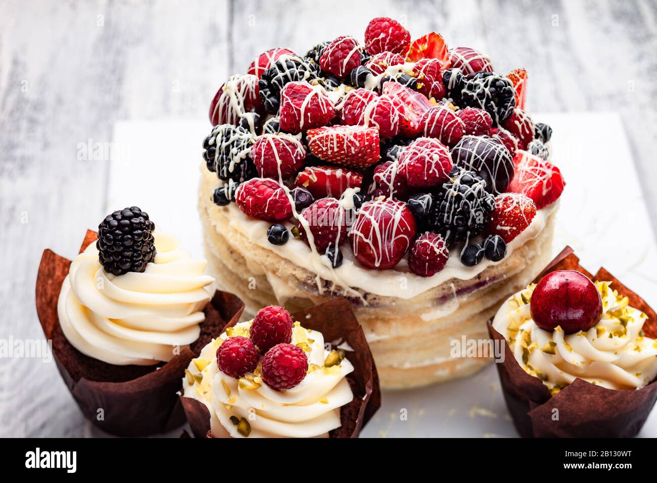Pfannkuchen mit einer Kappe Beeren, die in weißer Schokolade auf einem weißen Holztisch mit ein paar belgischen Muffins gedrillt ist Stockfoto