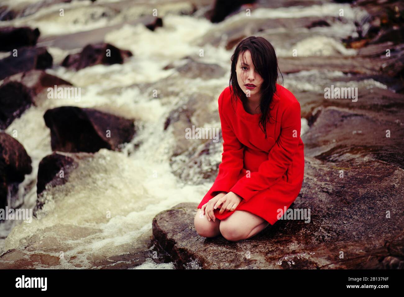 Junge Frau sitzt an einem Bach Stockfoto