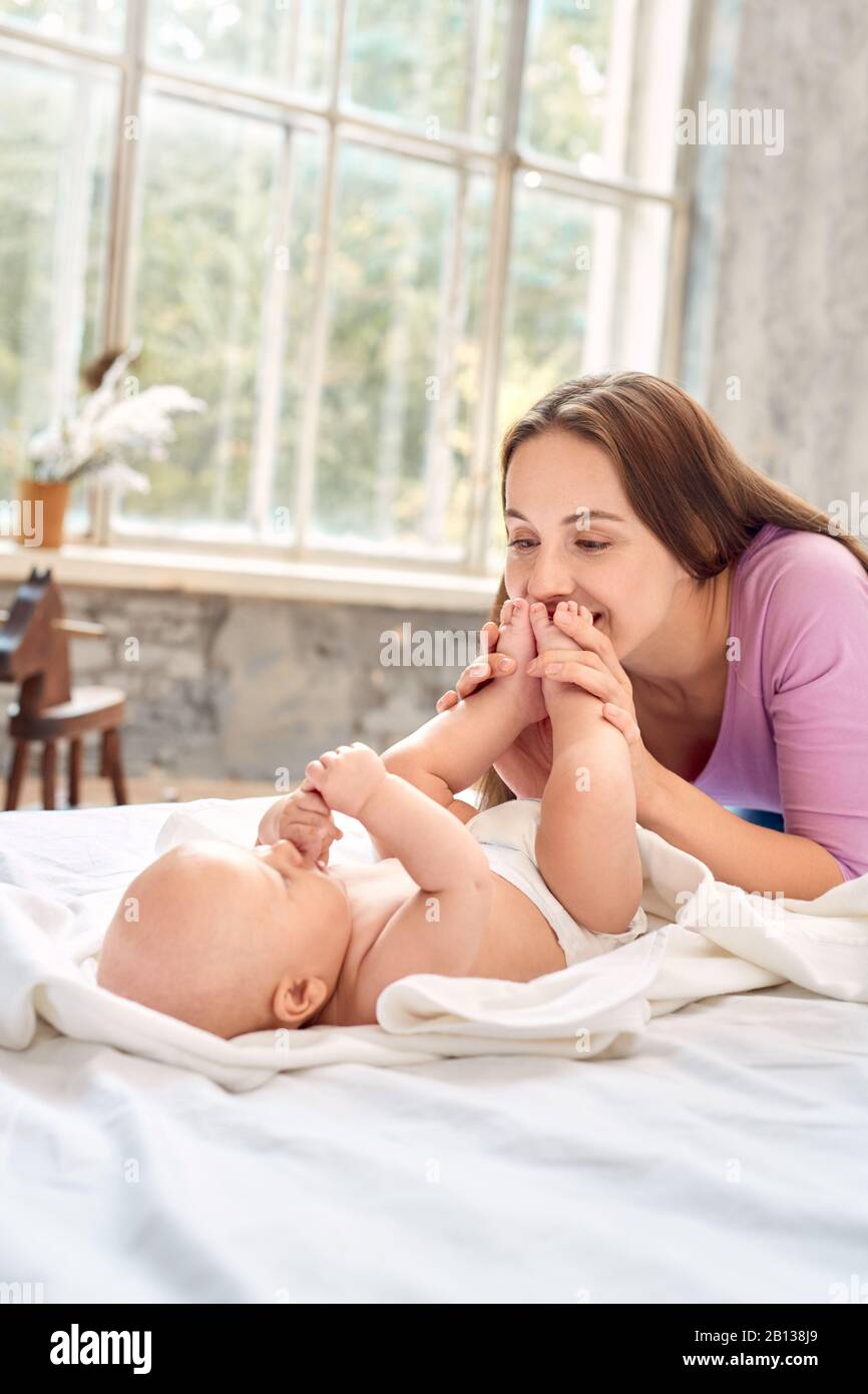 Junge Erwachsene Mutter, die ihre Füße küsst, ihr kleines neugeborenes Baby Stockfoto