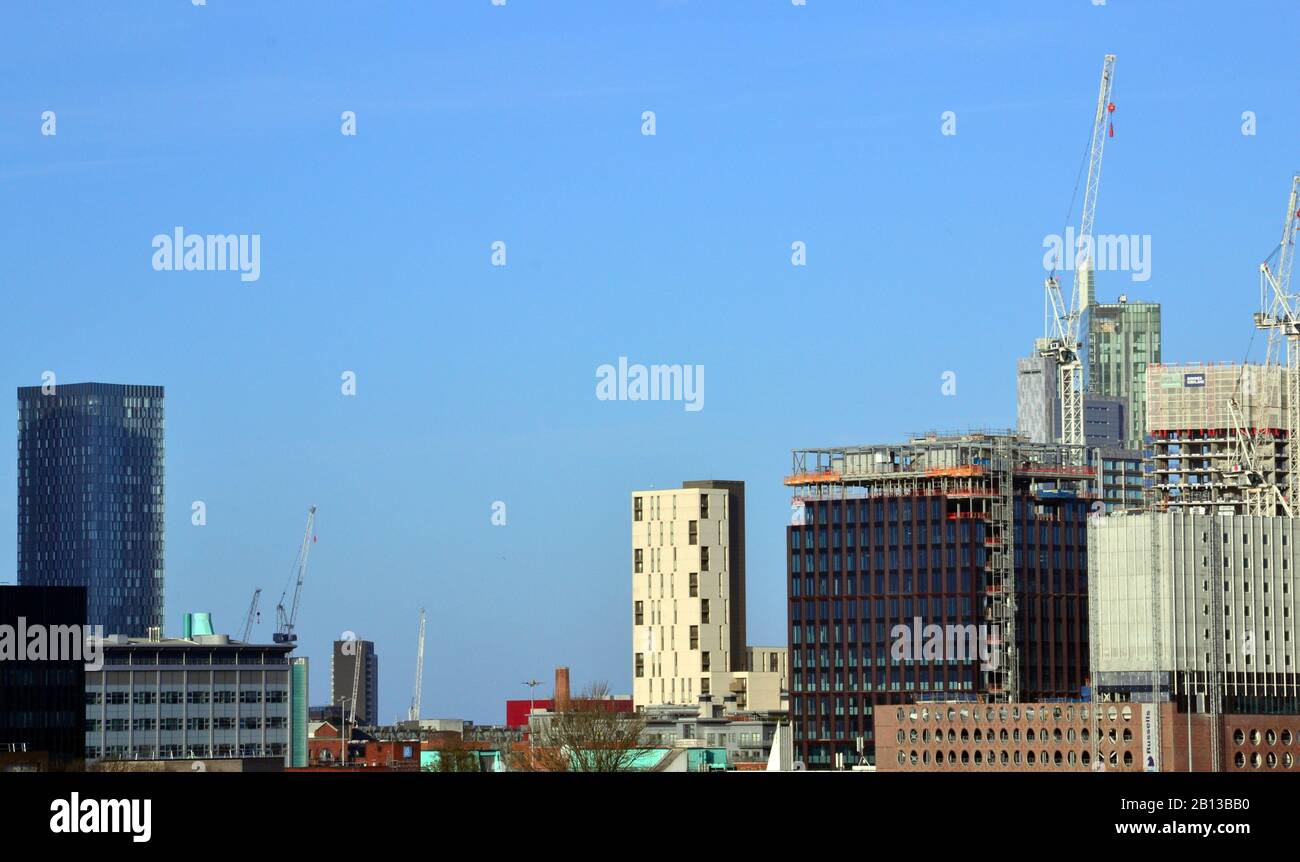 Hochhäuser, darunter einige im Bau befindliche Hochhäuser mit Turmkränen, im Zentrum von Manchester, Großbritannien, mit blauem Himmel dahinter. Stockfoto