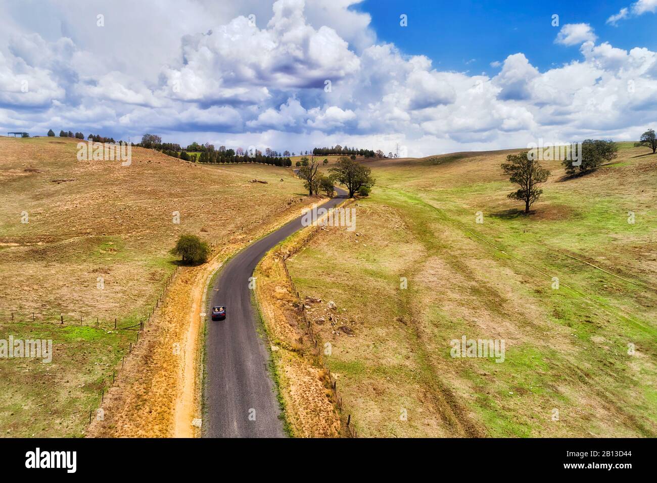 Trockene Landwirtschaft Rinderfarmen in den Blue Mountains in australien. Abgelegene einspurige Straße mit einem einsamen modernen, konvernierbaren Auto, das bergauf fährt. Stockfoto