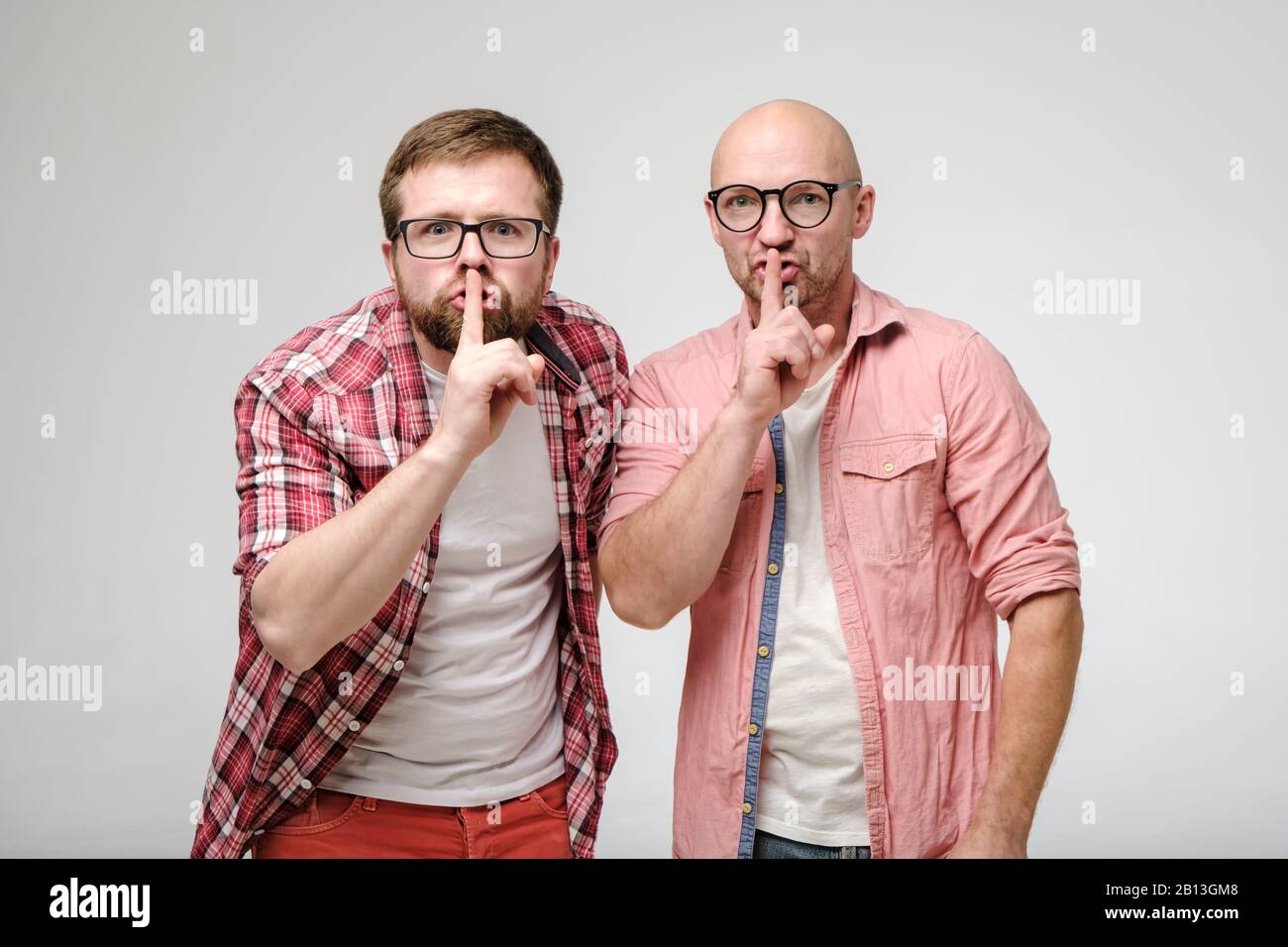 Zwei Männer sagen Schweigen, indem sie eine Geste mit einem Zeigefinger auf den Lippen machen und aufgeregt auf die Kamera schauen. Geheimnis der Freunde. Shh. Stockfoto