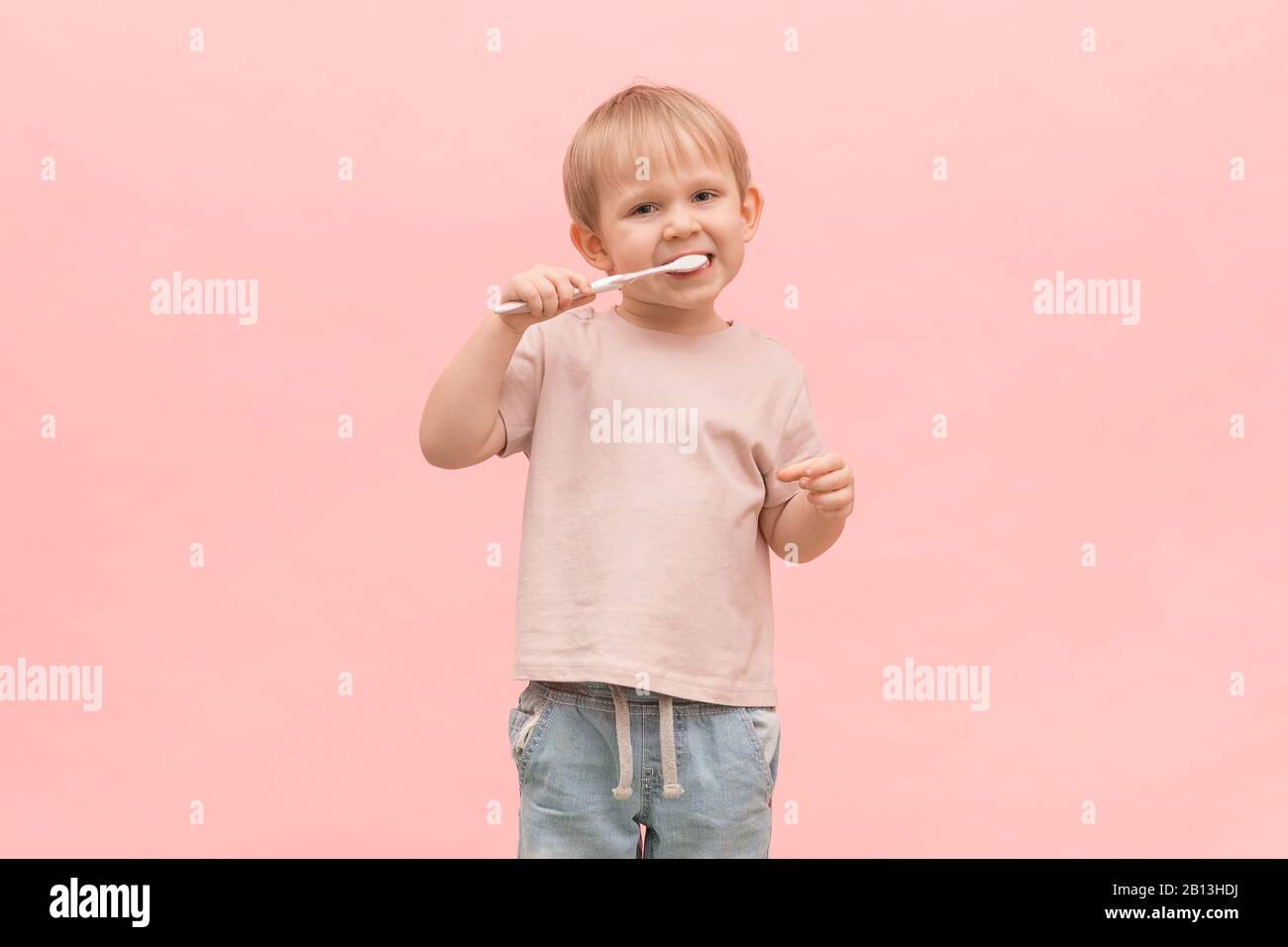 Blondine putzt seine Zähne mit einer Zahnbürste auf einem rosafarbenen Hintergrund. Konzept für Artikel über gesundes Zahnfleisch, Mundhygiene und Behandlung in Dentistr Stockfoto