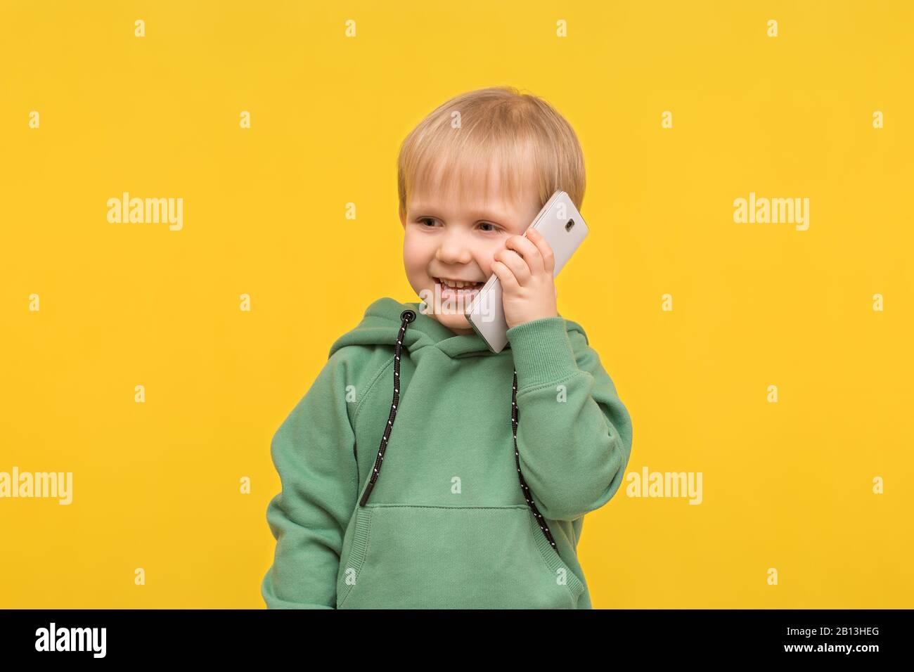 Kinderblonde spricht auf dem Telefon-Smartphone auf gelbem Federhintergrund. Konzept für Artikel über moderne Kindheit, Kinderkommunikation, Stockfoto