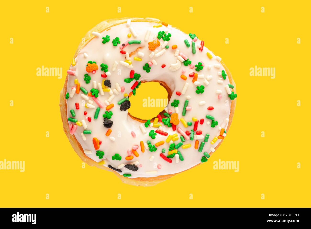 Köstliche Donuts mit weißer Frostfarbe und bunten Besprengungen auf hellgelbem Hintergrund. Große Nahaufnahme Stockfoto