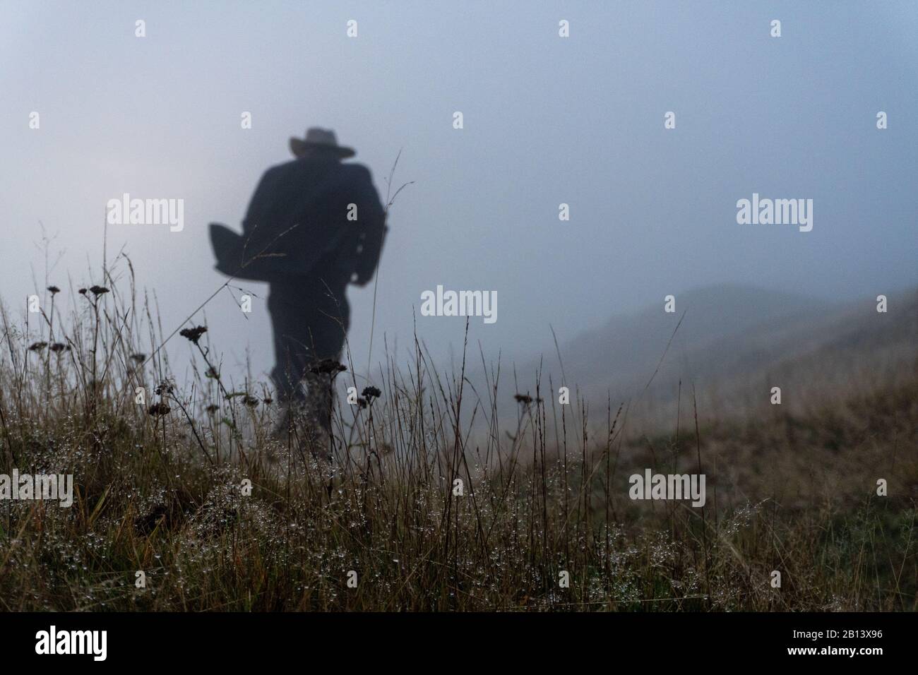 Film-noir-Konzept. Ein unscharfer, verschwommener Mann mit langem Mantel und einem Hut, der von der Kamera wegläuft, in Nebel geratene Silhouetten. Stockfoto