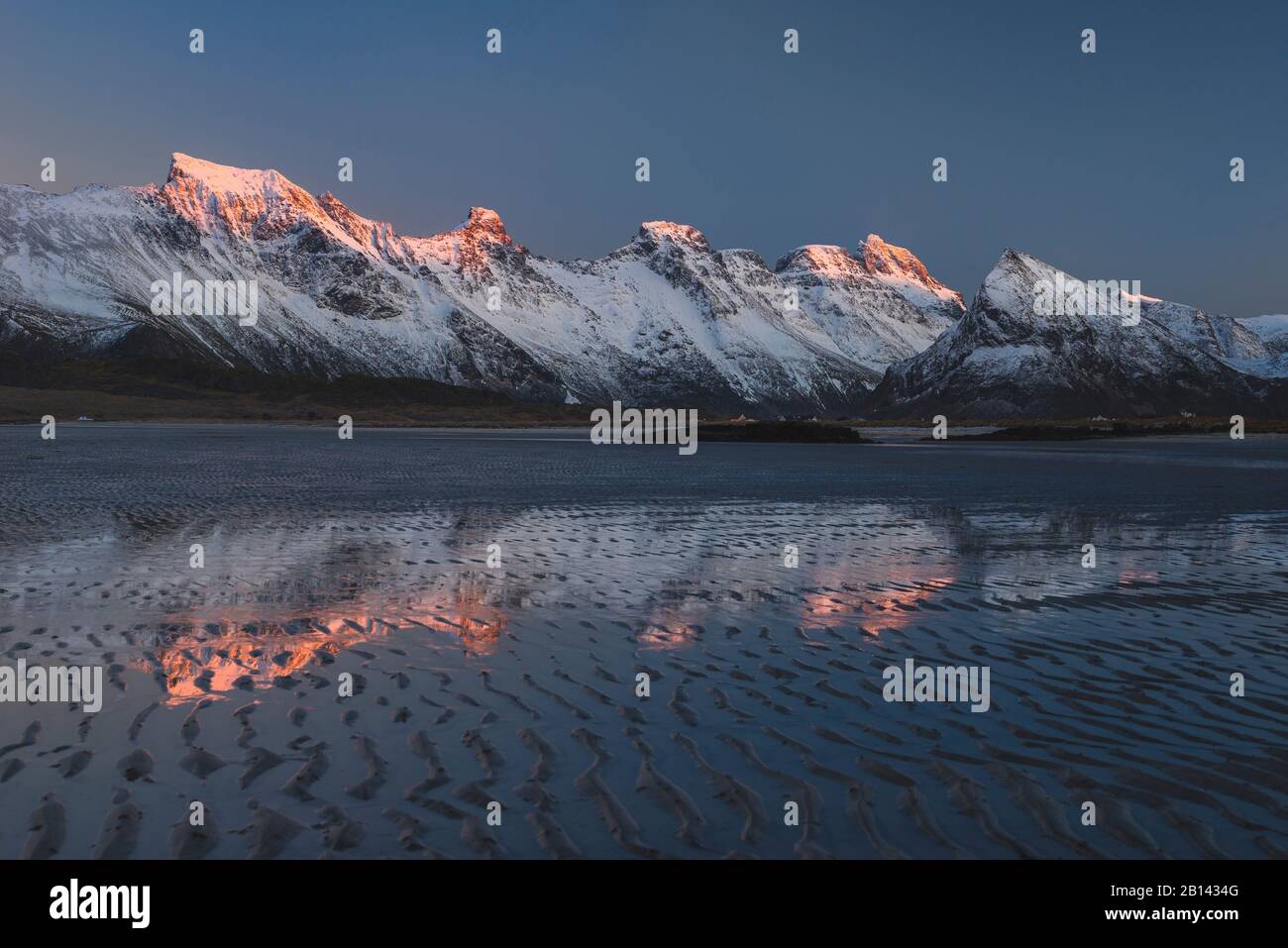 Letztes Licht auf den Gipfeln ist in den Pfützen auf dem Strand bei Ebbe, Lofoten, Nordland, Norwegen Stockfoto