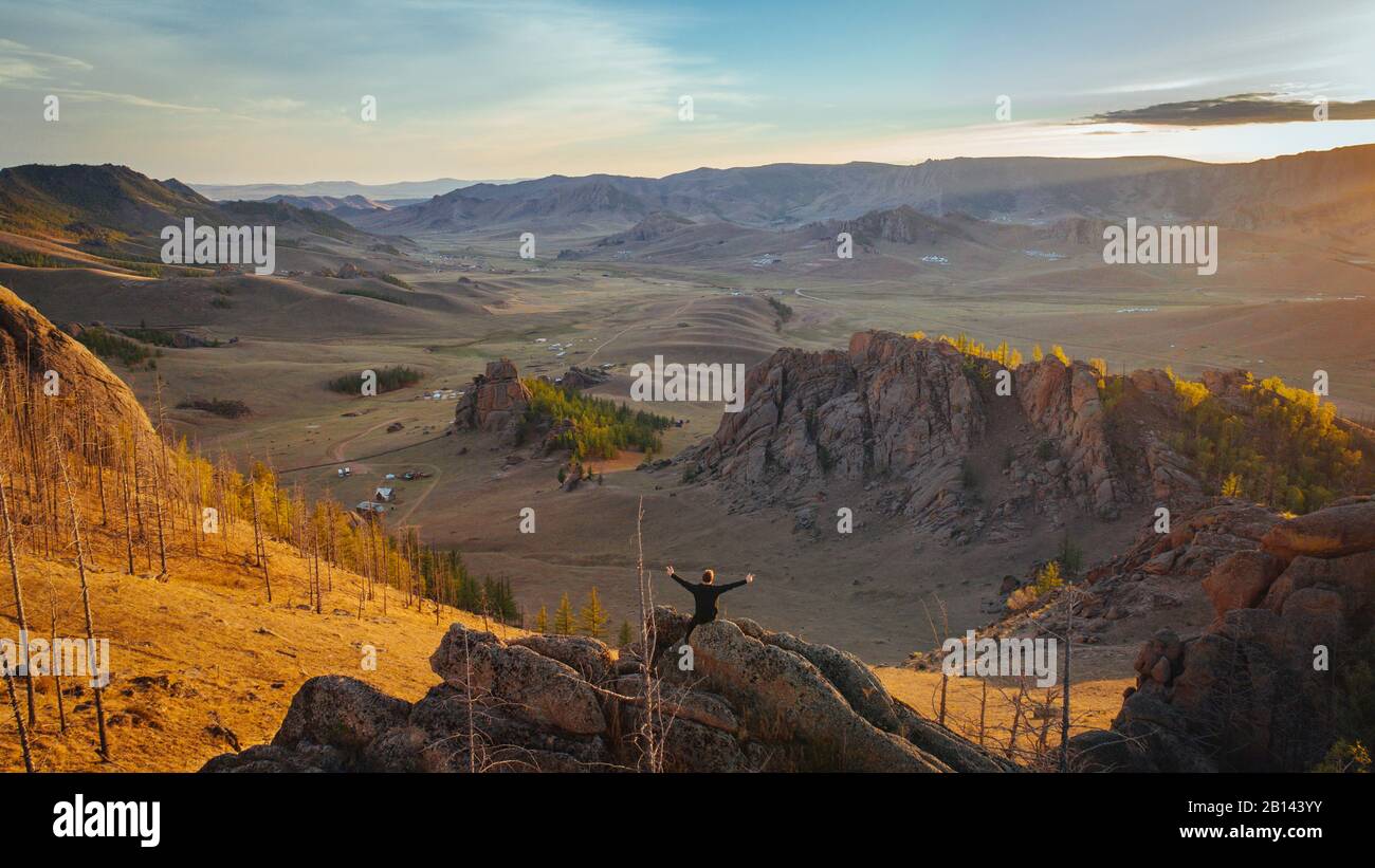 Mann sitzt auf Felsen mit ausgestreckten Armen, mongolische Schweiz, Wüste Gobi, Mongolei Stockfoto