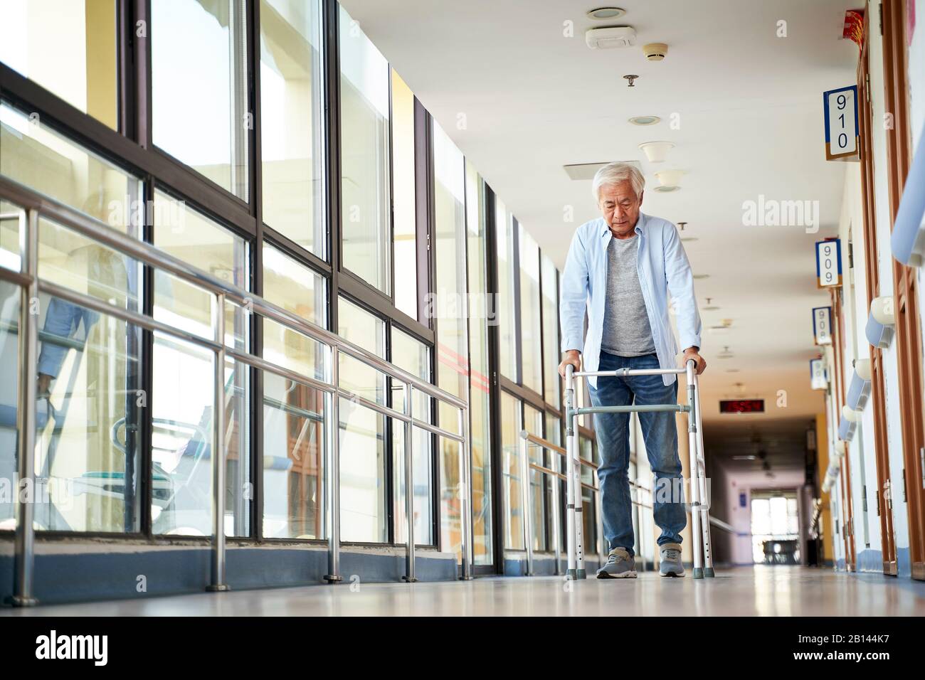 Leitender asiat, der mit einem Geher im Flur des Pflegeheims spazieren ging Stockfoto