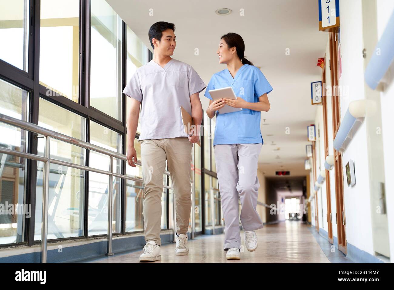 Fröhliche junge asiatische Physiotherapeuten, die im Flur des Pflegeheims spazieren gehen Stockfoto