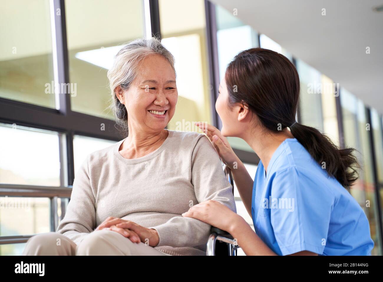 Freundliche Pflegekraft im Pflegeheim, die mit der asiatischen Seniorin im Flur spricht Stockfoto