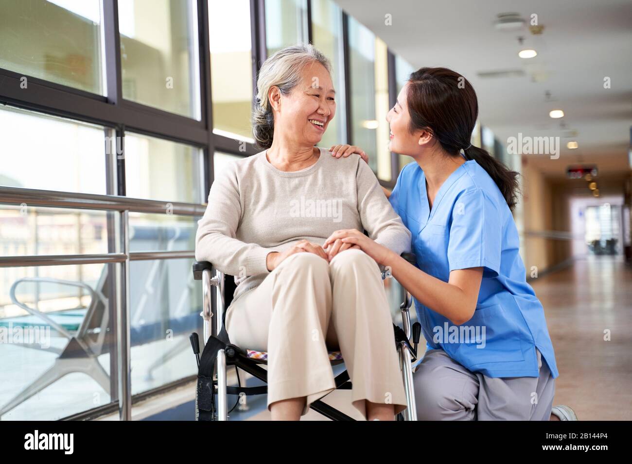 Freundliches Personal Pfleger des Pflegeheims spricht mit asiatischer Seniorin im Flur Stockfoto