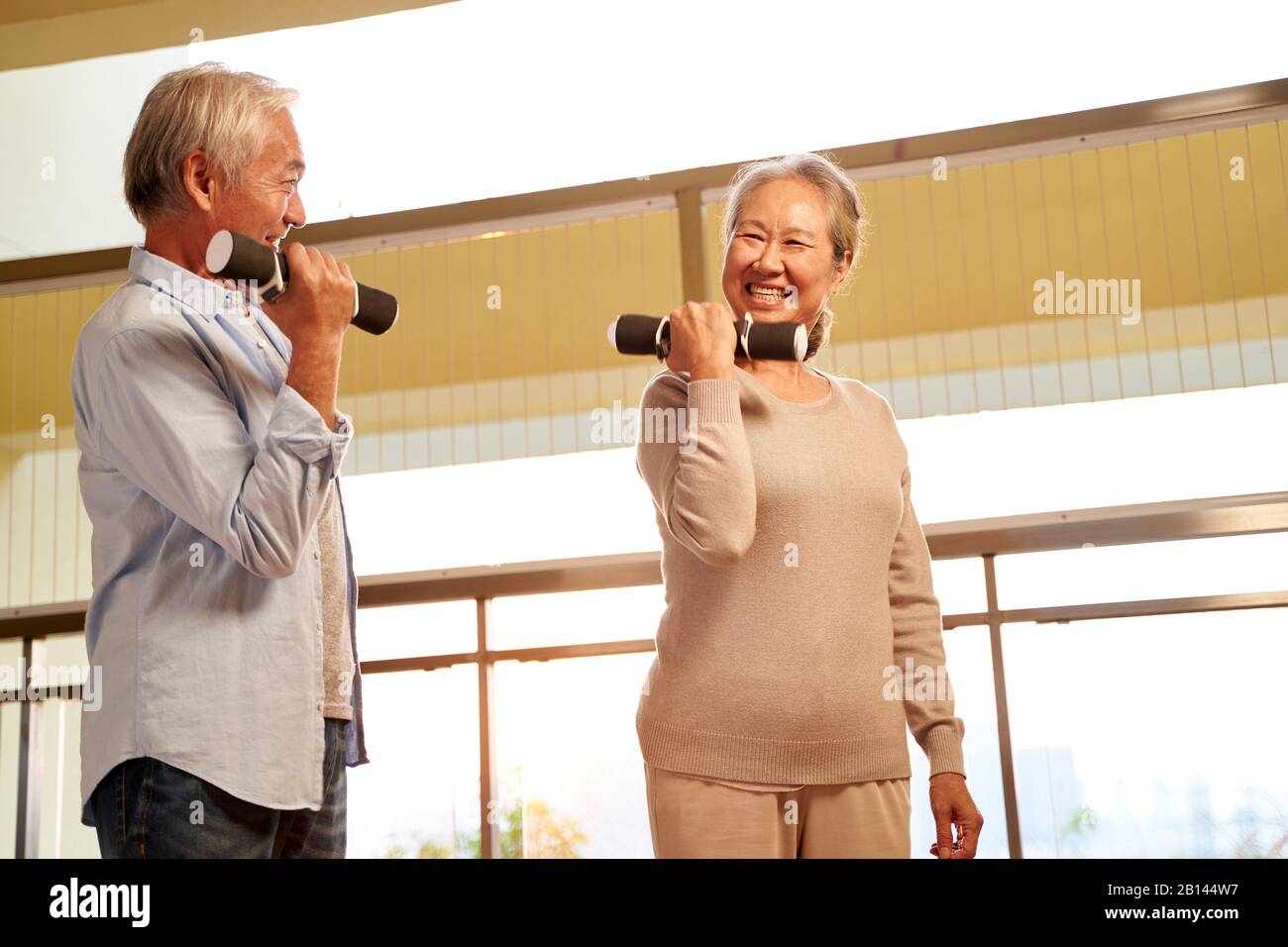 Glückliches älteres Paar aus asien, das mit Hanteln im Pflegeheim trainiert Stockfoto