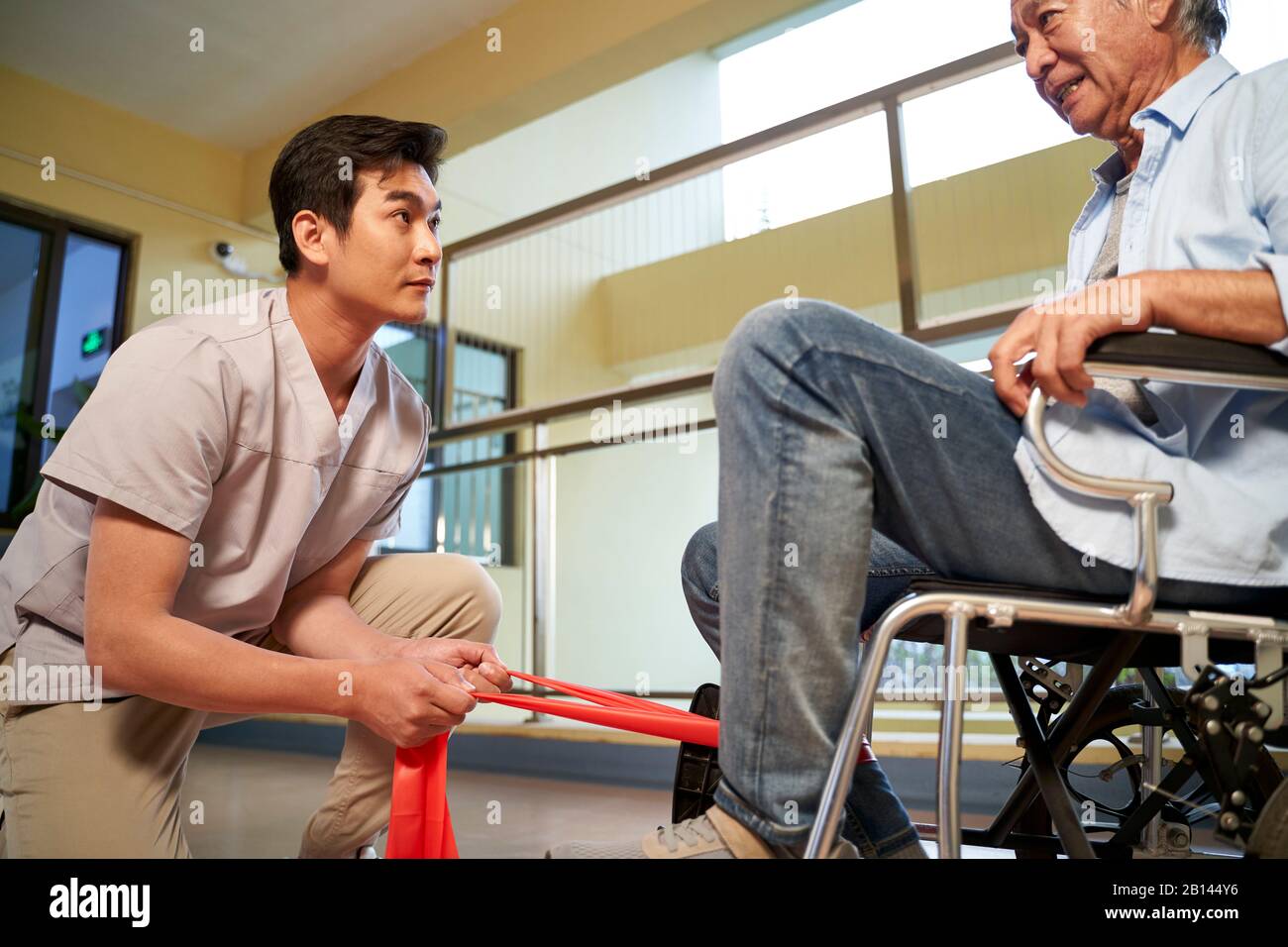 Junger asiatischer Physiotherapeut arbeitet mit dem Senior man an der Verbesserung der Beinstärke mithilfe eines Widerstandsbandes Stockfoto