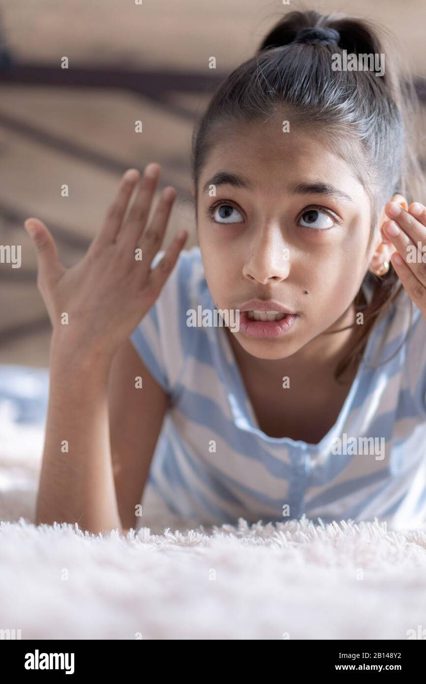 Das junge Mädchen aus dem mittleren Osten zeigt Empörung, liegt auf einem hellbeigen Bett im Licht des Sonnenlichts. Persisches swarthisches Mädchen auf dem Bett. Mitte Stockfoto