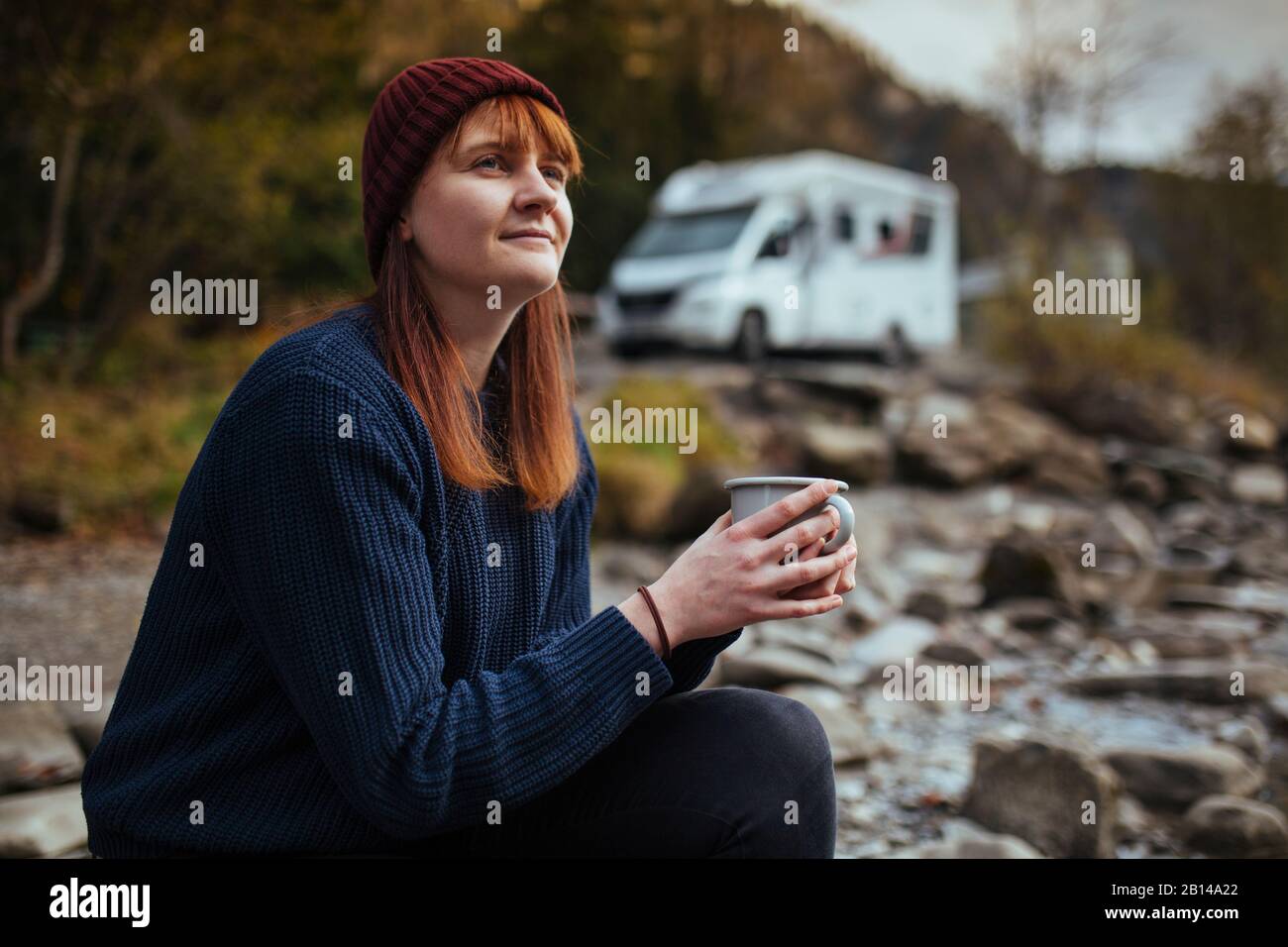 Road Trip l Frau sitzt mit einer Tasse Tee vor dem Wohnmobil Stockfoto