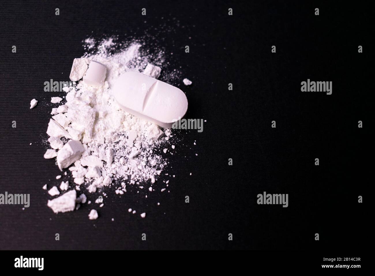 Zerdrückte Tablette auf schwarzem Hintergrund. Kopierbereich. Konzept des Drogenmissbrauchs Stockfoto