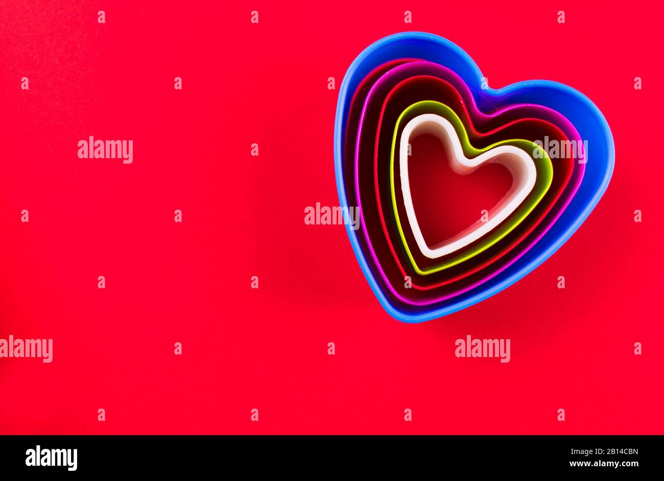Plätzchenschneider in Form von Herzen unterschiedlicher Größe auf rotem Hintergrund. Kopierbereich. Stockfoto