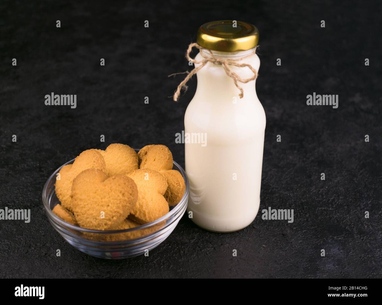 Flasche mit Milch und herzförmigen Plätzchen auf schwarzem Hintergrund. Kopierbereich. Stockfoto