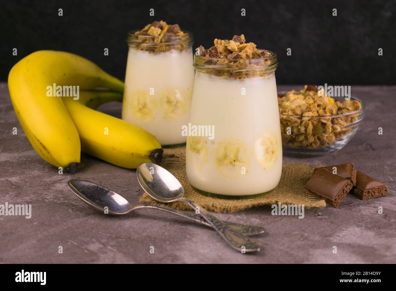 Zwei Gläser mit Bananenjoghurt und Granola auf grauem Hintergrund. Granola, gesundes Frühstück. Stockfoto
